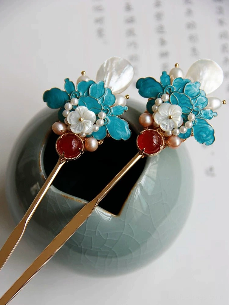 Matching blue peony Chinese hair sticks with gold-tone metal shafts, pearls, white shell flowers, and red agate details displayed beside a ceramic vase