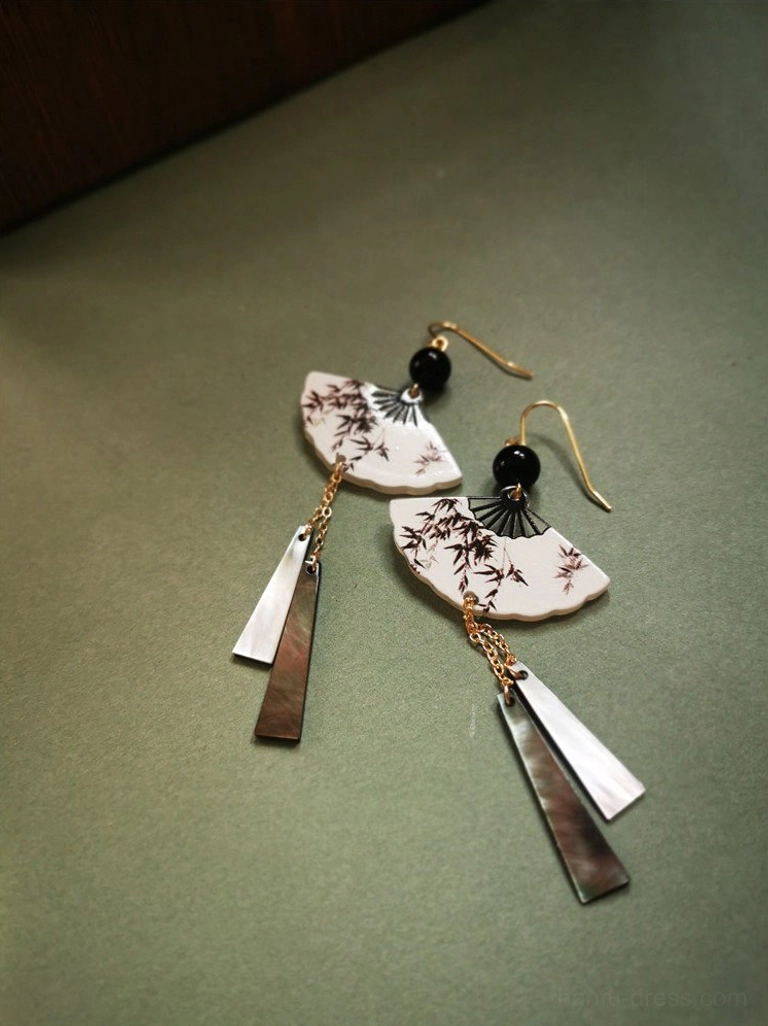 Matching brown bamboo fan-shaped Chinese drop earrings with gold ear hooks and long dual-tone metal tassels on a dark green background