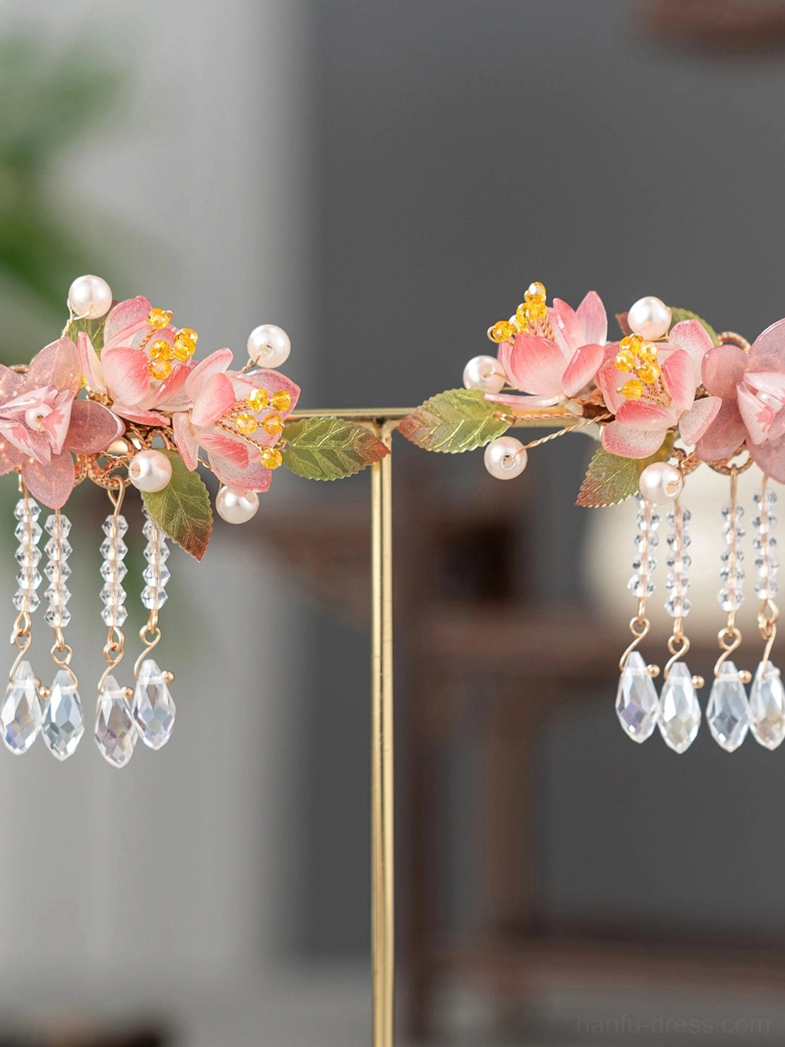 Pair of matching Chinese-style cherry blossom Hanfu hair clips with pink flowers, white pearls, gold chains, and dangling crystal tassels on a decorative stand