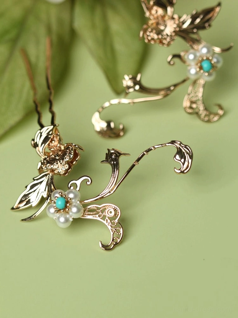 Pair of matching gold-toned Chinese hair pins with floral designs, imitation pearl centers, and turquoise-colored accents shown on a light green decorative background
