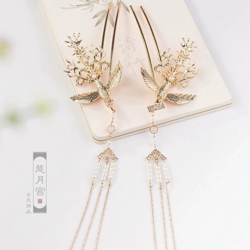 Matching pair of traditional Chinese golden phoenix hairpins with pearl-style tassels arranged on a vintage Chinese-style notebook