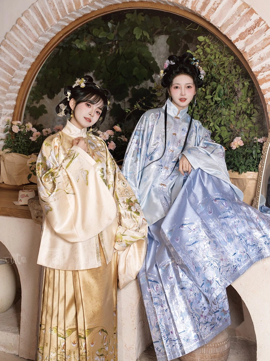 Two models wearing coordinated Ming Dynasty-inspired Hanfu clothing with embroidered pipa sleeve tops and silky golden pleated mamianqun skirts