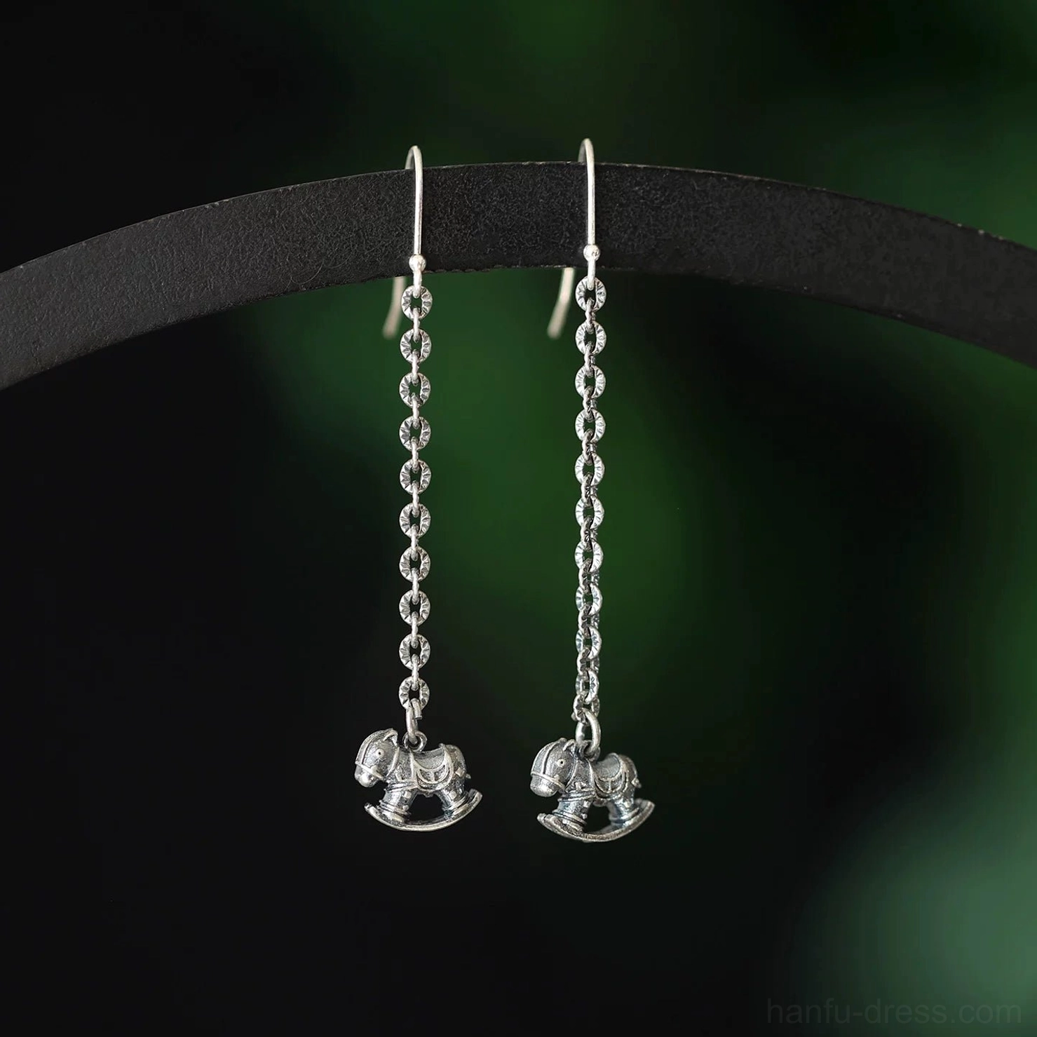 Matching pair of polished silver rocking horse hook earrings with symmetrical twisted chain details displayed on a black jewelry rod