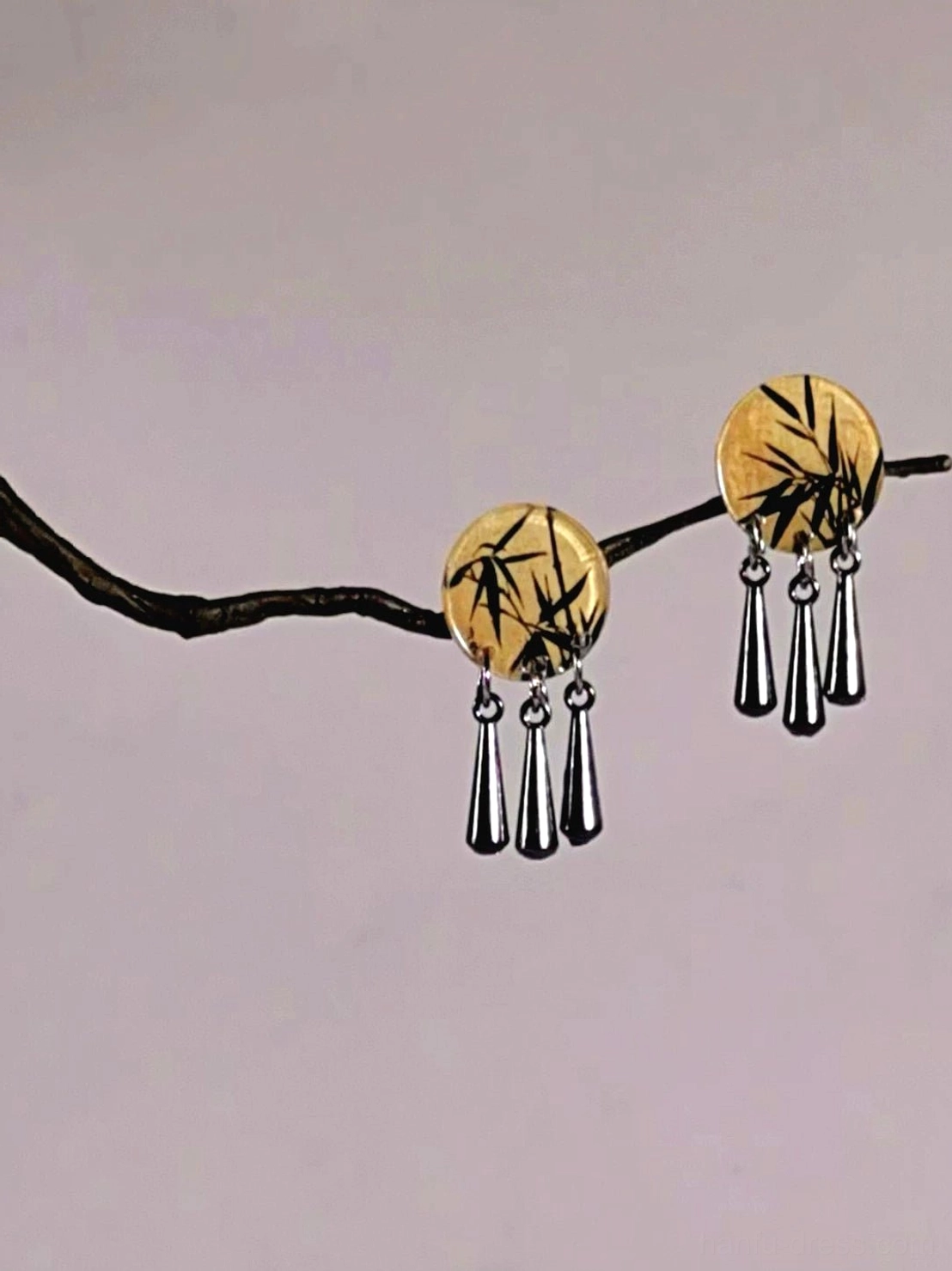 Matching pair of Chinese-inspired bamboo dangle earrings displayed on a branch with round bamboo print charms and silver teardrop pendants