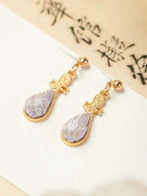 Matching pair of purple pipa-shaped Chinese earrings arranged on vintage Chinese calligraphy paper, showing carved lute details gold ear posts and embroidered fabric pendants