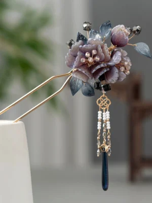 Mauve peony Chinese hair stick with blue resin leaves, gold-toned double prongs, beaded tassel, dark blue pendant, and Chinese knot charm displayed on a white stand