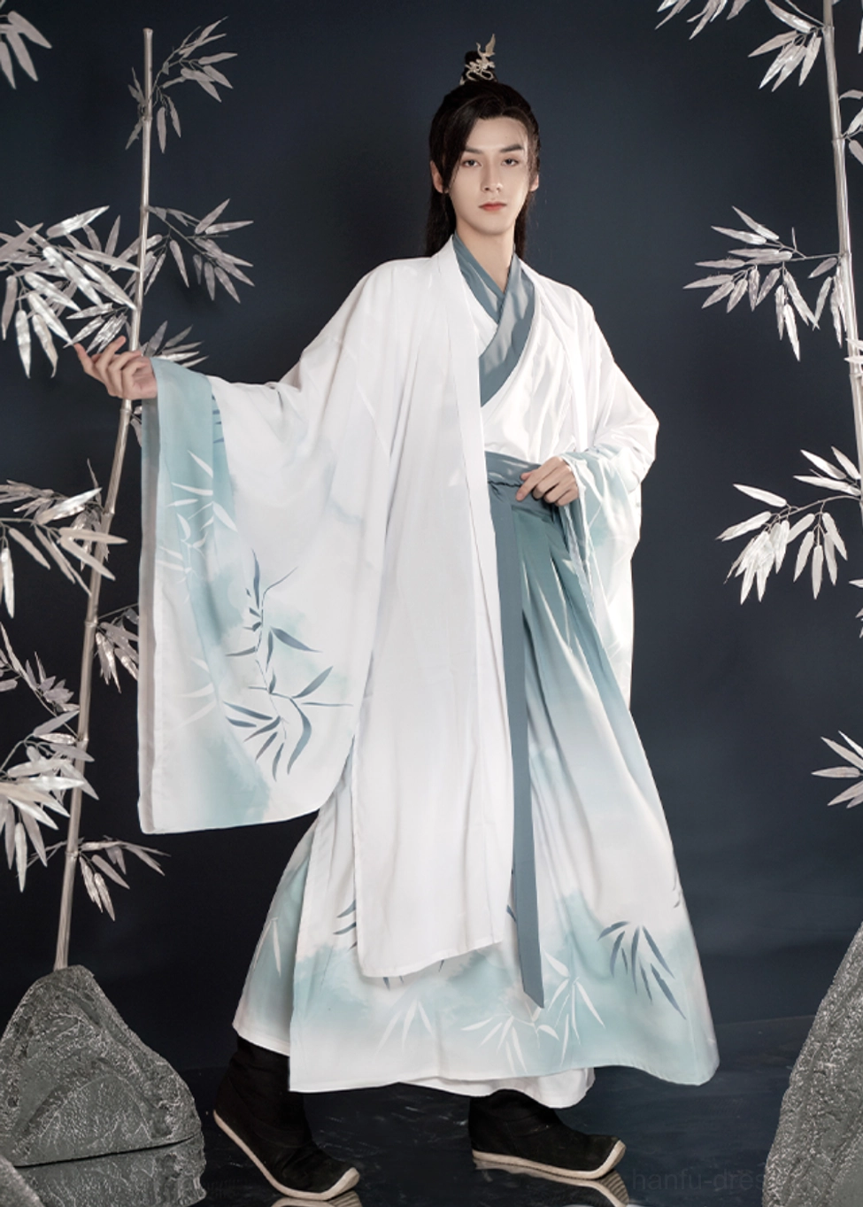 Full-body three-quarter front view of a male model wearing Bamboo Rhyme men's Hanfu with a white to turquoise gradient, printed bamboo leaves, cross-collar top, wrap skirt, and wide-sleeved outer robe
