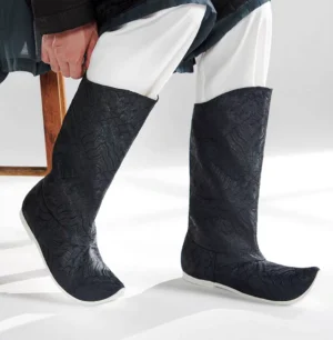 Side view of men's black brocade Chinese Hanfu tall boots with embossed texture, upturned pointed toes, white rubber soles, and a traditional historical-inspired silhouette