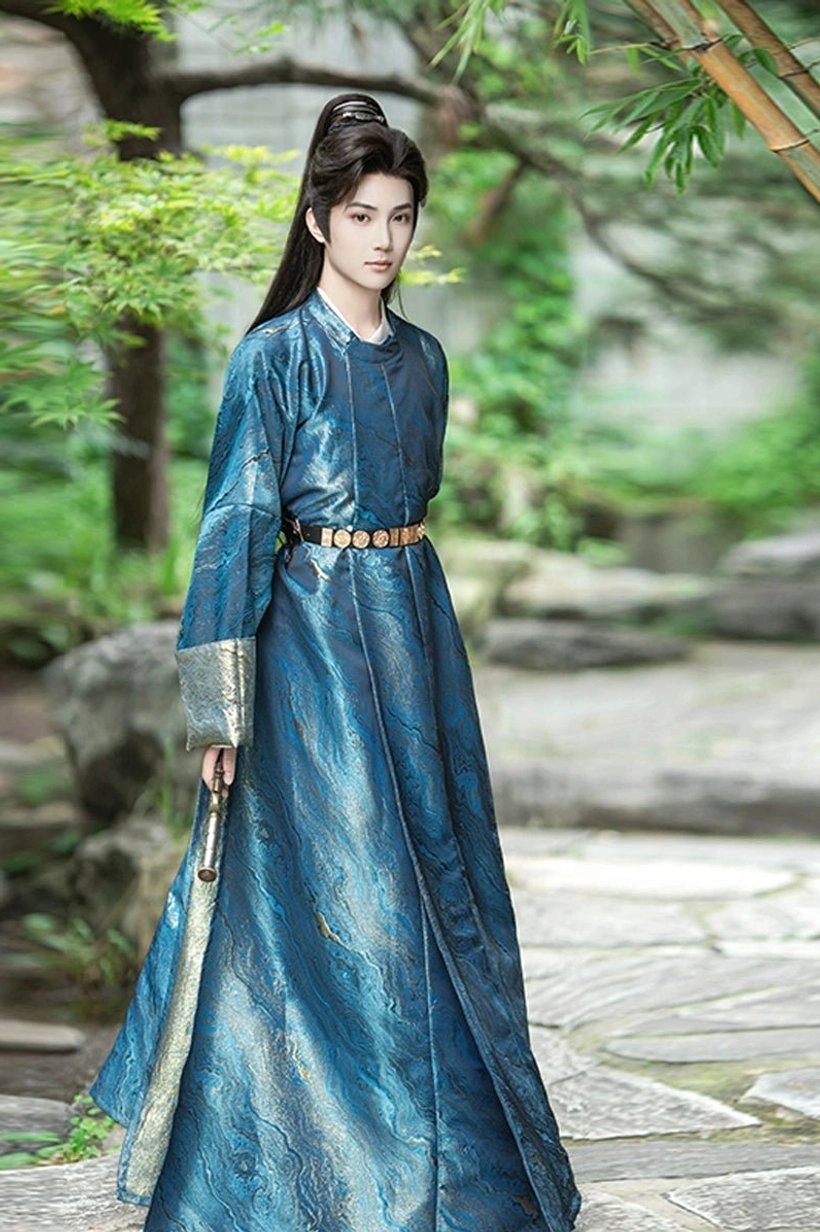 Full-body side view of a man wearing a deep blue men's round-collar Hanfu robe with gold decorative waist belt, gold cuffs, and long sword in a classical garden