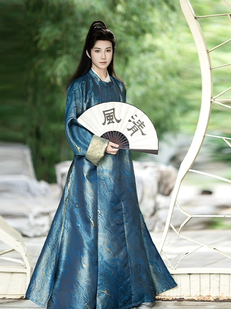 Full-body front view of a man wearing a deep blue men's Tang-style Hanfu robe with gold cuffs, flowing floor-length silhouette, folding fan, and ancient Chinese hairstyle