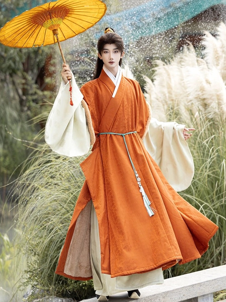 Three quarter view of flowing burnt orange men’s Ming style winter Hanfu robe with soft cream cuff trim in a reed garden