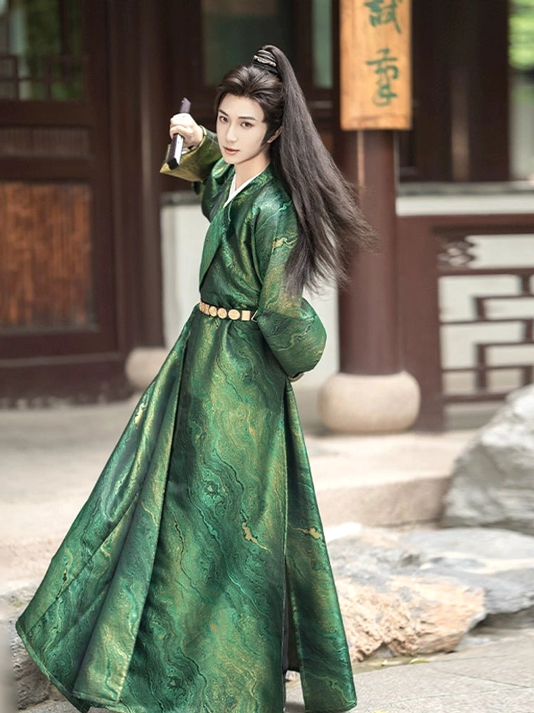 Men's dark green cross-collar-inspired Hanfu robe with textured water-wave pattern, golden waist belt, and decorative handheld sword in a traditional wooden courtyard
