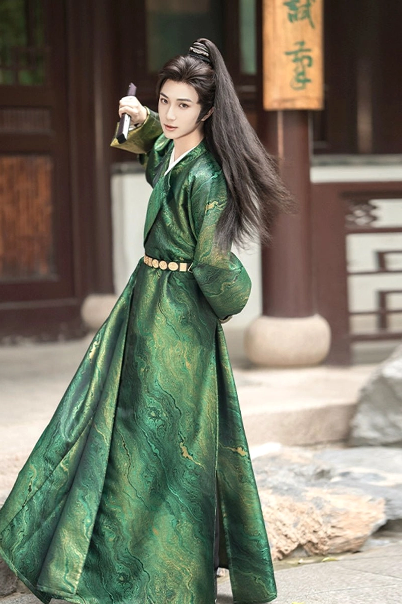 Side view of a man wearing a dark green men's Tang-style Hanfu robe with water-wave jacquard texture, gold waist belt, and small traditional sword at a wooden courtyard