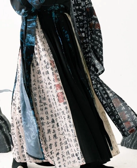 Close up detail of a men’s Hanfu lower garment showing ancient Chinese calligraphy prints, blue decorative patterns, layered black fabric, and flowing outer robe