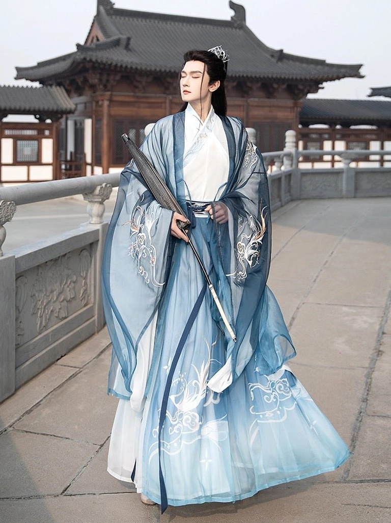 Heather blue men's wuxia Hanfu Qiyao Ruqun set with flowing gradient robes and silver mythical bird embroidery worn in a traditional Chinese courtyard