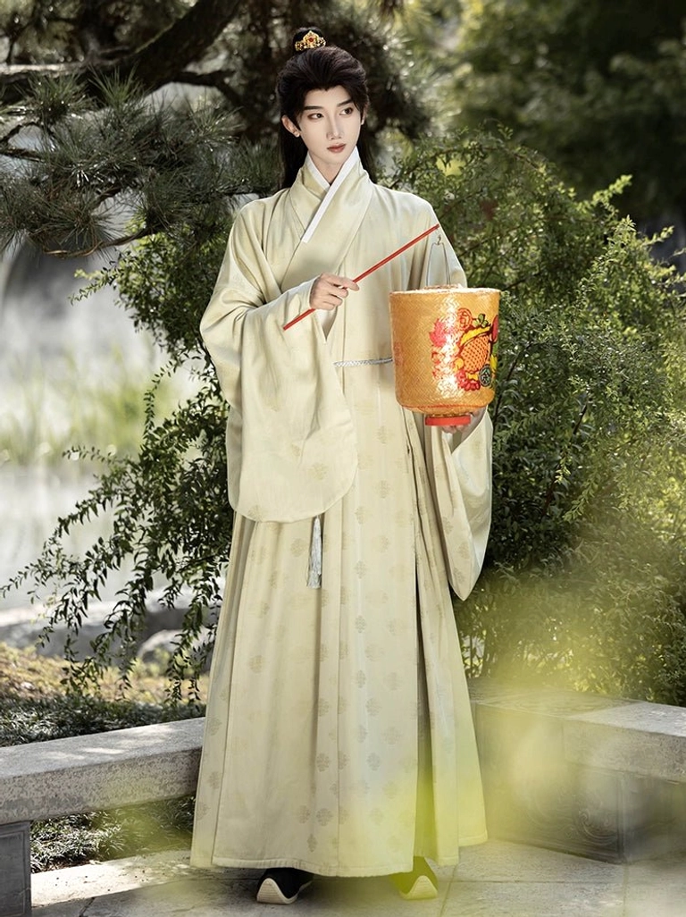 Male model in cream beige Ming style Hanfu inner robe with subtle jacquard pattern holding a lantern beside a pine garden