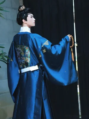 Rear three-quarter view of royal blue men’s Ming style Hanfu yuanlingpao robe with wide sleeves, white belt, and embroidered back buzi