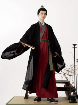 Three-quarter view of a man wearing traditional Song Dynasty-style hanfu with wide flared sleeves, patterned collar and cuffs, layered black robe, burgundy inner robe, and folding fan