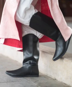 Side close-up of a men's Tang Dynasty Hanfu boot in bright black microfiber leather with a high shaft and pointed flat toe, styled with pink traditional Chinese clothing