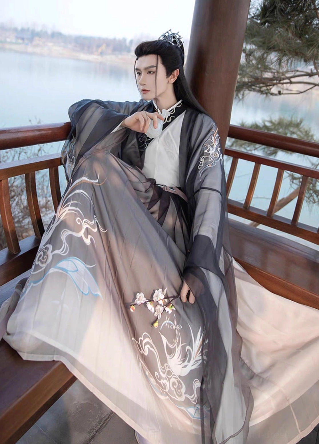Seated close-up of men's Thunder black wuxia Hanfu showing detailed silver embroidery flowing gradient hem and layered Qiyao Ruqun styling by a lake
