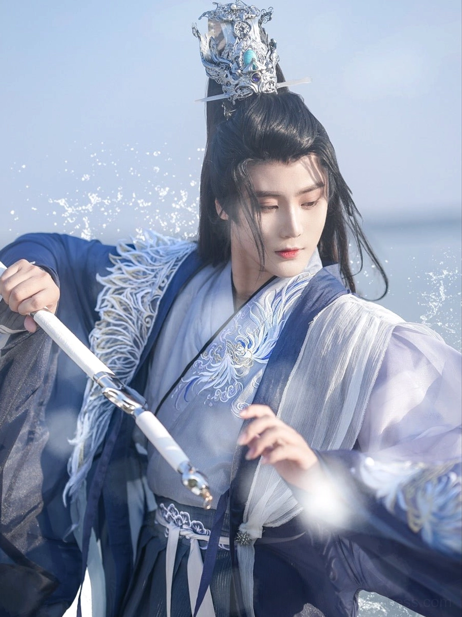 Upper-body close-up of a male model wearing embroidered cross-collar wuxia hanfu with white feather shoulder decoration, silver hair crown, and ceremonial sword