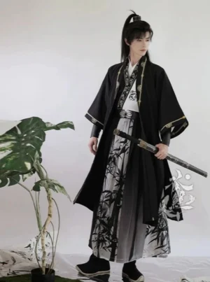 Full-body front view of a men's wuxia Hanfu set with black outer robe, gold trim, ink bamboo print, and gradient wrap skirt