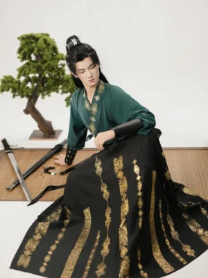 Male model wearing a dark green and black wuxia Hanfu outfit with embroidered collar and patterned wrap skirt while seated beside traditional swords
