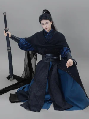 Three quarter kneeling view of a men's Xianxia hanfu set with flowing black robe, navy inner layer, chiffon shoulder wrap, and sword styling