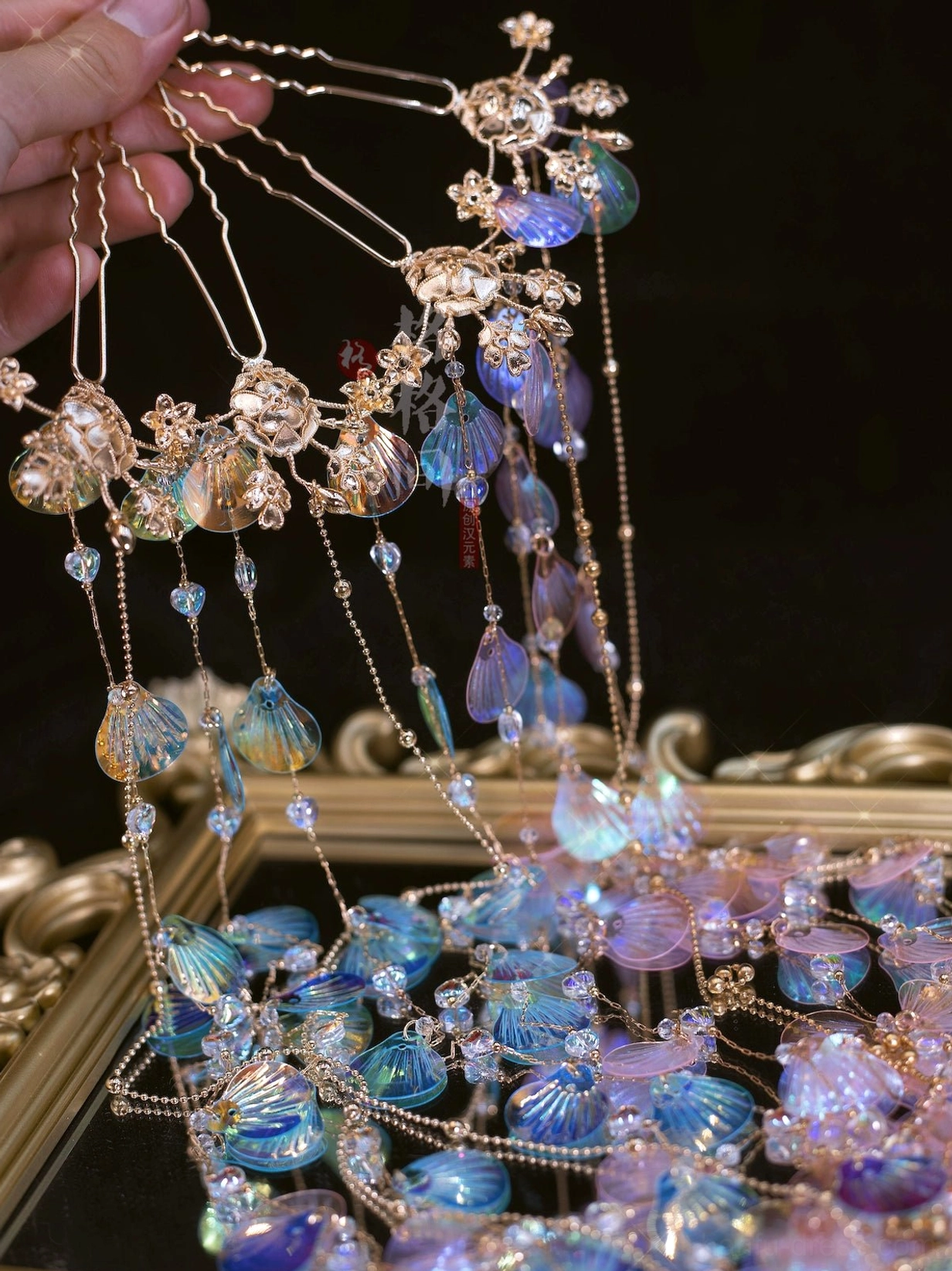 Close-up of iridescent blue purple mermaid shell tassel Hanfu hair pins with gold flower mounts and delicate beaded chains held in hand