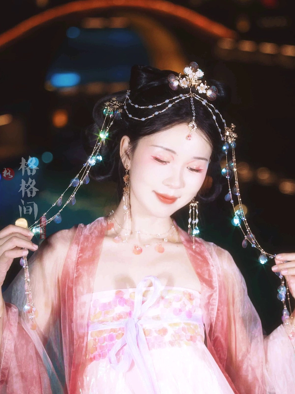 Model in pink traditional Hanfu wearing mermaid shell tassel hair accessories with gold floral details during an evening riverside portrait