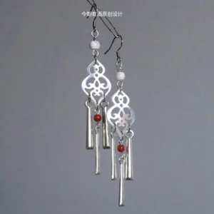 Close-up of Miao ethnic style hollow carved gourd drop earrings with hook closures, white bead accents, red details, and layered silver-toned tassel pendants for Hanfu and Qipao