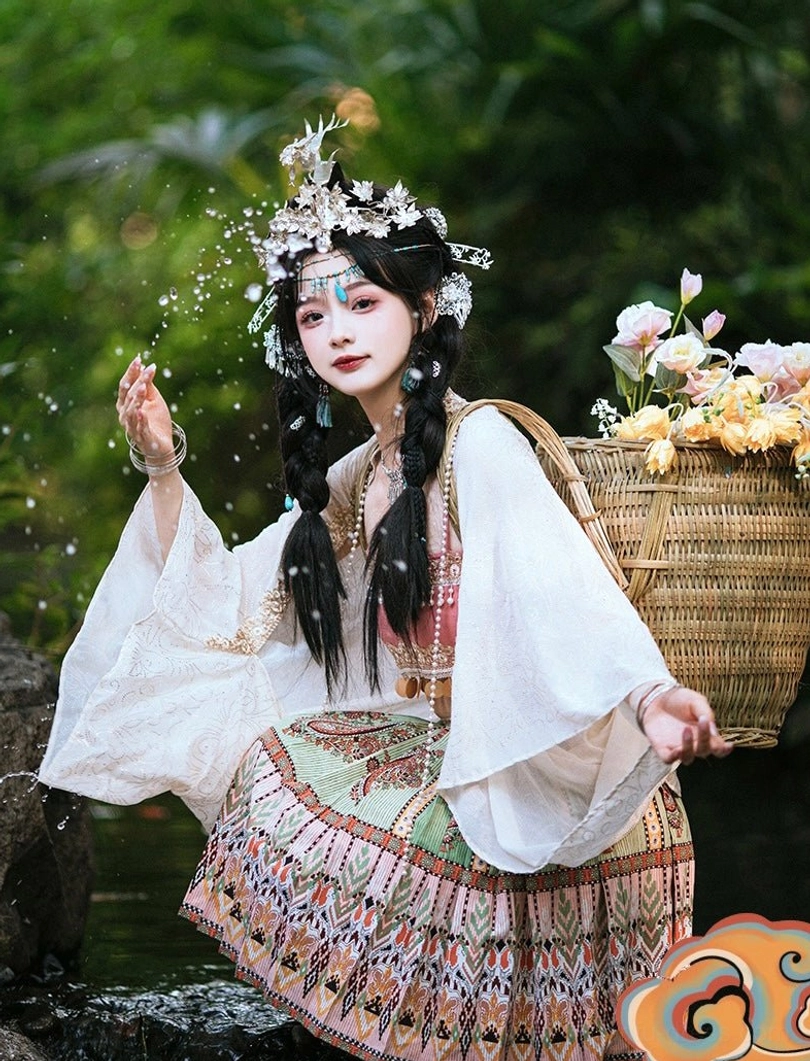 Side view of a pink and ivory Miao inspired modern Hanfu set with ethnic patterned pleated skirt silver headdress and floral wicker backpack
