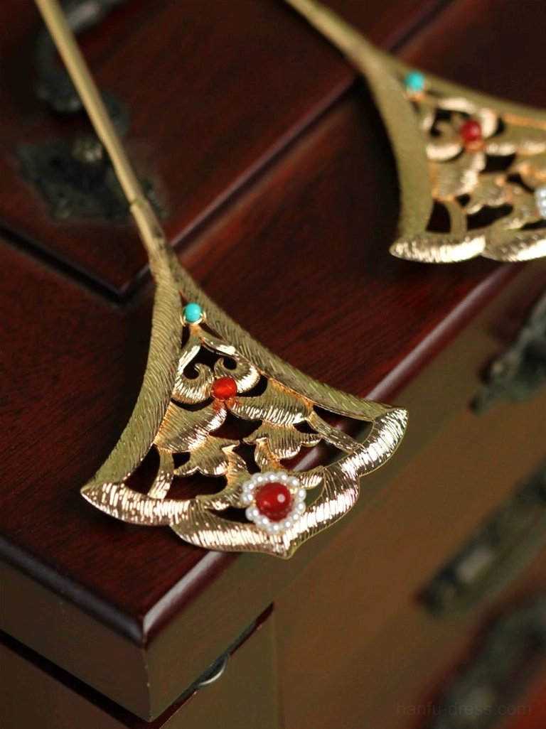 Two gold ginkgo leaf Chinese hair pins displayed on a dark wooden surface with carved metal details, red beads, turquoise beads, and pearl accents