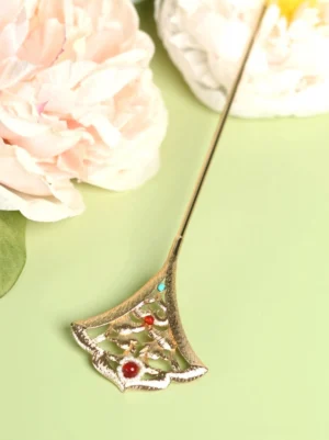 Close-up of a gold-toned Miaoling ginkgo leaf Hanfu hair pin with openwork floral carving, red beads, turquoise accents, and white pearl details arranged beside pink peony flowers