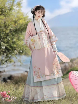 Pink Ming Dynasty Hanfu set with floral embroidered robe and blue pleated mamian skirt shown in a spring flower meadow