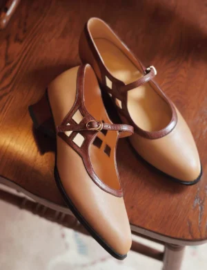 Pair of milk tea vintage Chinese Mary Jane shoes displayed on a wooden chair, featuring two-tone brown design, geometric T-strap cutouts, adjustable ankle buckles, pointed toes, and low block heels