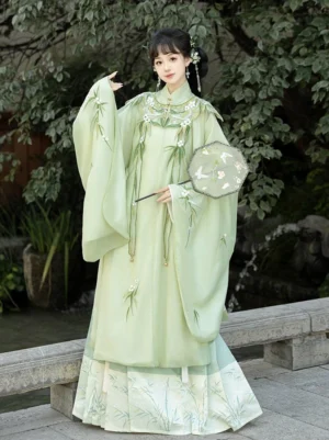 Front view of a sage green Ming Dynasty Hanfu set with bamboo leaf embroidery, cloud collar, flowing robe, and mamian skirt in a classical Chinese garden