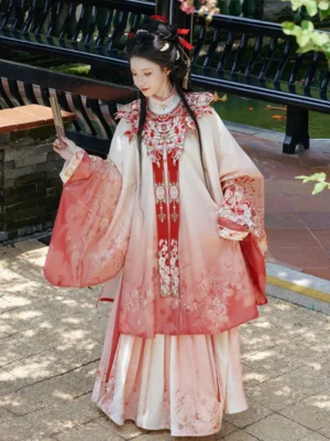 Three-quarter front view of a woman wearing a Ming Dynasty hanfu set with cream to rose red ombre fabric, embroidered cloud collar, floral and butterfly-inspired details, and flowing wide sleeves on a classical Chinese garden path