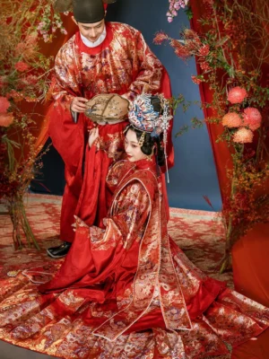 Ming Dynasty Chinese wedding Hanfu couple set in red and gold, bride and groom posing in a traditional red floral wedding studio