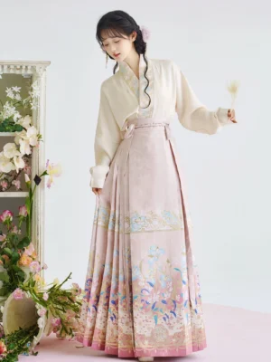 Three-quarter front view of beige cross-collar Ming Dynasty Hanfu top with pink iris floral mamian skirt and gold trim
