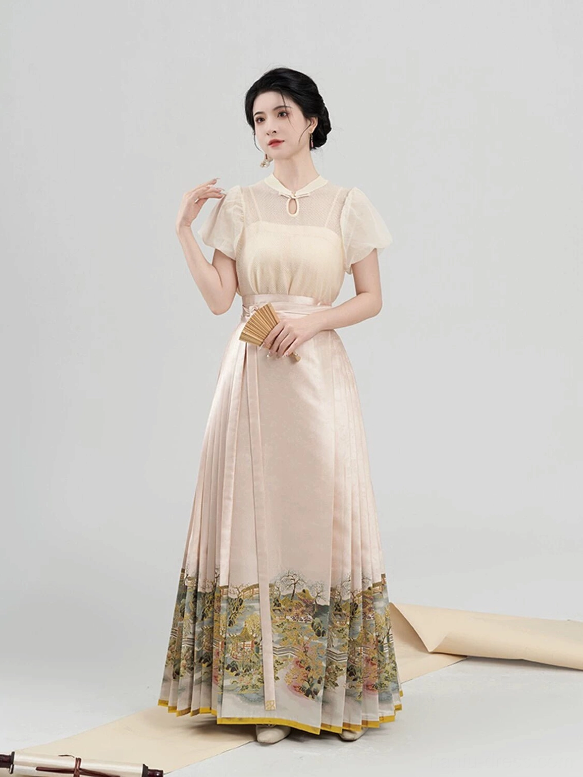 Full front view of a modern Ming Dynasty inspired hanfu blouse and mamian horse-face skirt outfit in apricot beige with sheer puff sleeves and a scenic landscape print hem