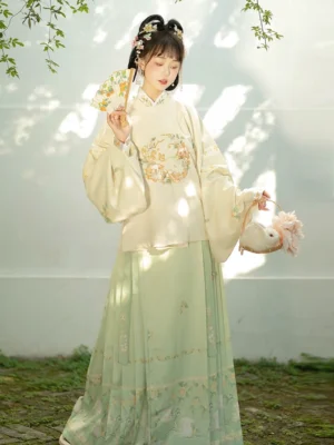 Full front view of a cream Ming Dynasty hanfu pipa sleeve top with floral embroidery and light green rabbit print mamianqun skirt in a sunny Chinese garden