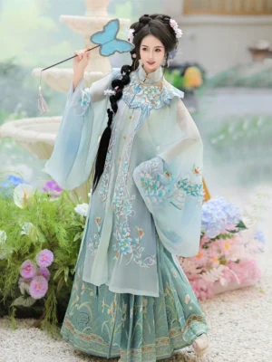 Ming Dynasty Hanfu woman wearing a light cyan embroidered robe, teal mamian skirt, and floral cloud collar in a colorful outdoor garden