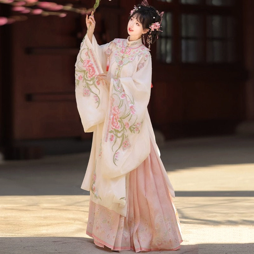 Ming Dynasty Hanfu full set shown from a low angle with cream floral embroidered robe and flowing pink pleated skirt in a courtyard