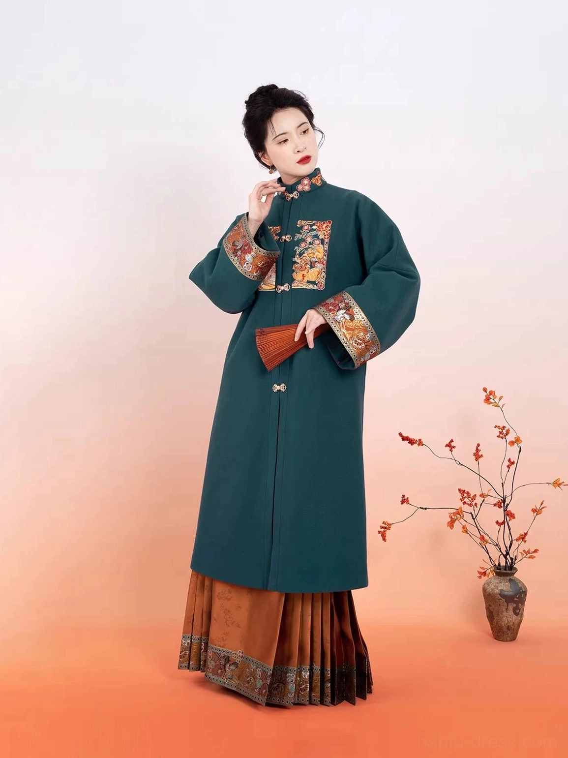 Three-quarter view of a traditional Ming Dynasty Hanfu outfit with a dark teal embroidered robe and brocade mamianqun skirt styled with a folding fan