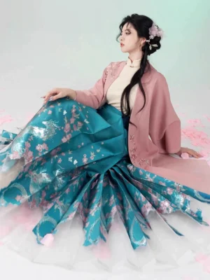 Three-piece Ming Dynasty inspired hanfu outfit with pink outer coat beige mandarin collar blouse and teal embroidered mamian skirt shown in a graceful seated studio portrait