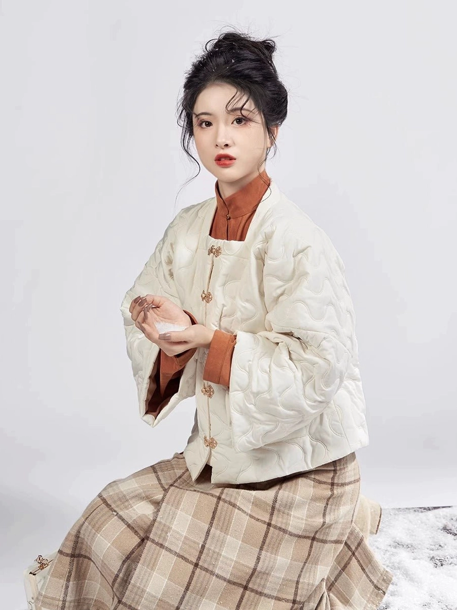 Half-body seated view of the Ming Dynasty Hanfu outfit showing the cream quilted jacket traditional frog buttons layered cuffs and caramel inner top