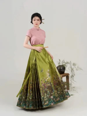 Model wearing an olive green Ming Dynasty style mamian skirt with floral and bird printed hem, pink stand collar Chinese blouse, matching waist ties, and traditional Chinese hairstyle