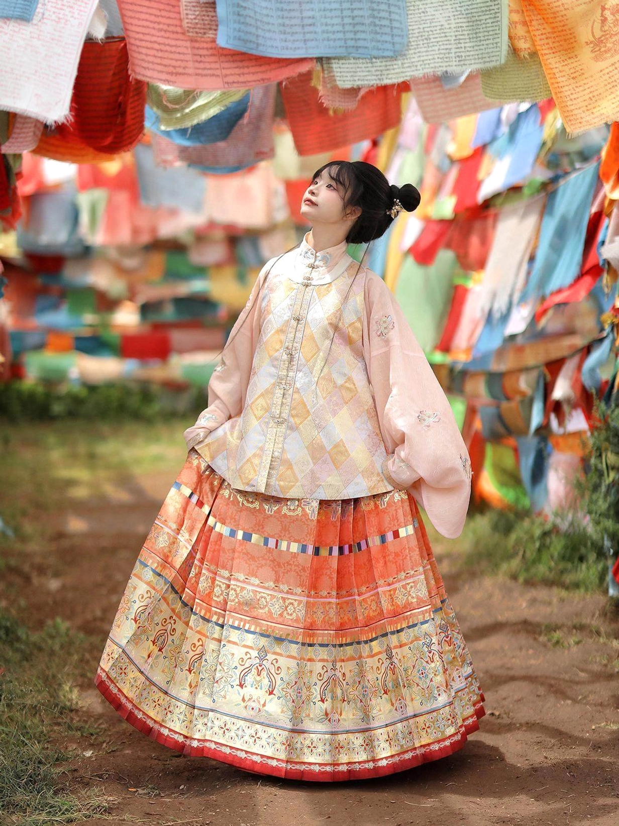 Pastel orange Ming Dynasty hanfu set with pipa sleeve top and pleated mamian skirt photographed outdoors with colorful prayer flags