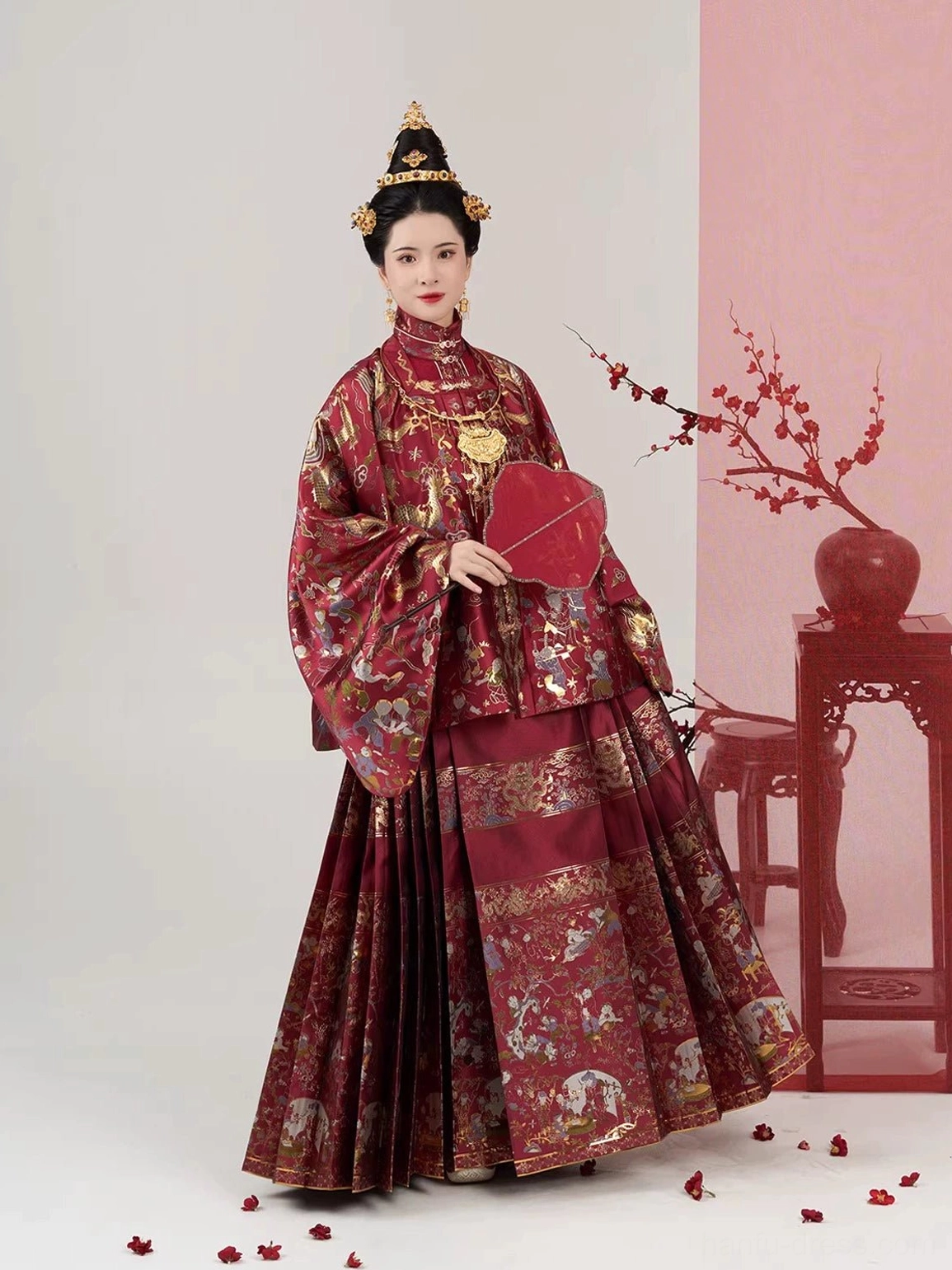 Red Ming Dynasty bridal Hanfu with pleated Mamian skirt, traditional wedding hair ornaments, and red silk fan shown from the right side